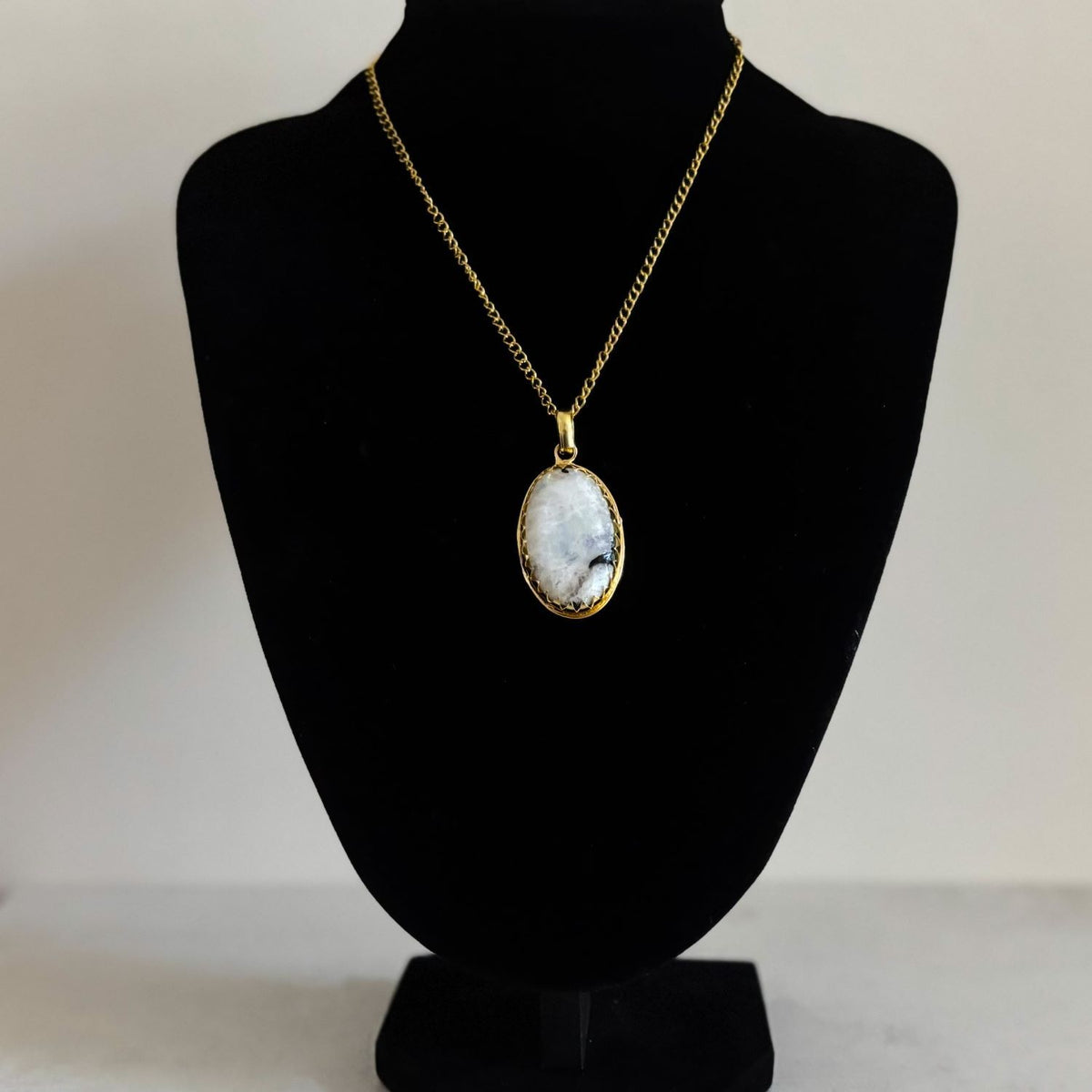 Rainbow moonstone pendant necklace on a gold curb chain, displayed on a black velvet bust for drape and scale