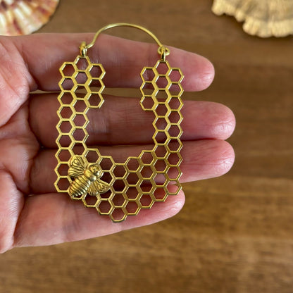 Close-up of honeycomb lattice and sculpted bee on Honeycomb Bee Brass Hoop Earrings, held in hand for scale