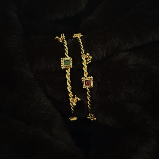 Twisted Brass Kada Bangle Pair with Ghungroo — Jhanak in gold-polished brass with red and green glass by Boho Mantra