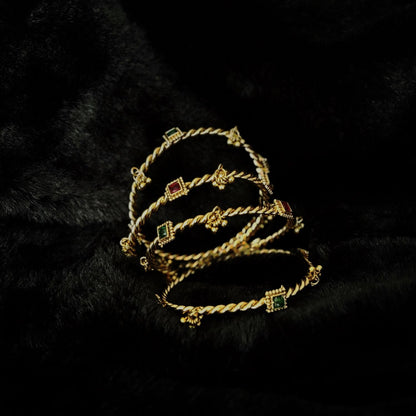Two pairs of Jhanak twisted brass kada bangles at an angle, showing the slim rope band and bell clusters